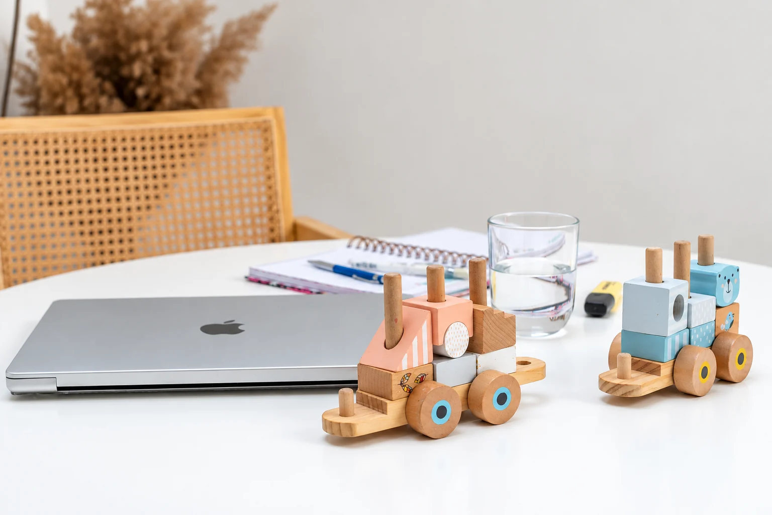 Un portátil, un cuaderno y juguetes de madera comparten la mesa de trabajo
